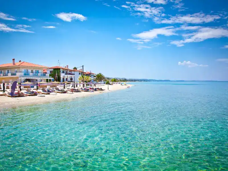 crystal clear waters of the sea with a white sand coastline and two houses in the background