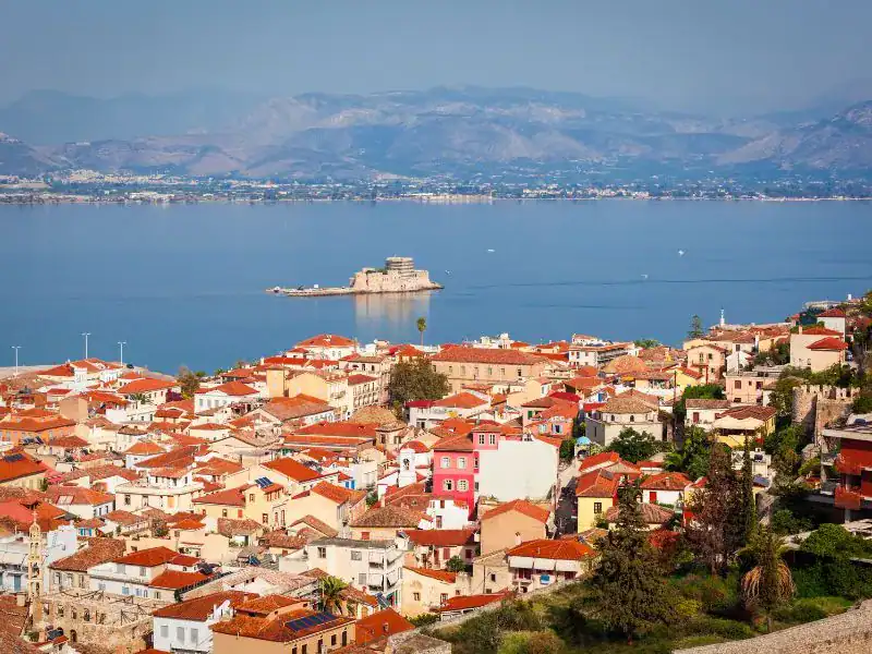 realistic photo of a city next to the sea with a lot of houses with red tile roofs