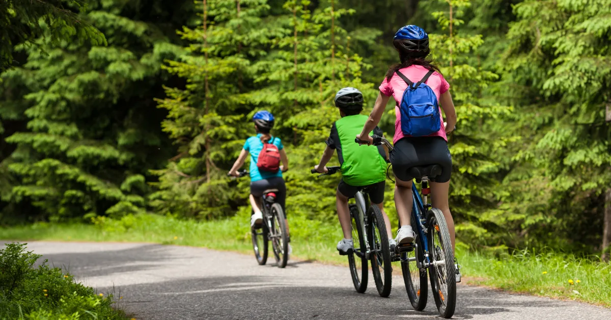 realistic photo of a three people riding a bicycle in a forest road